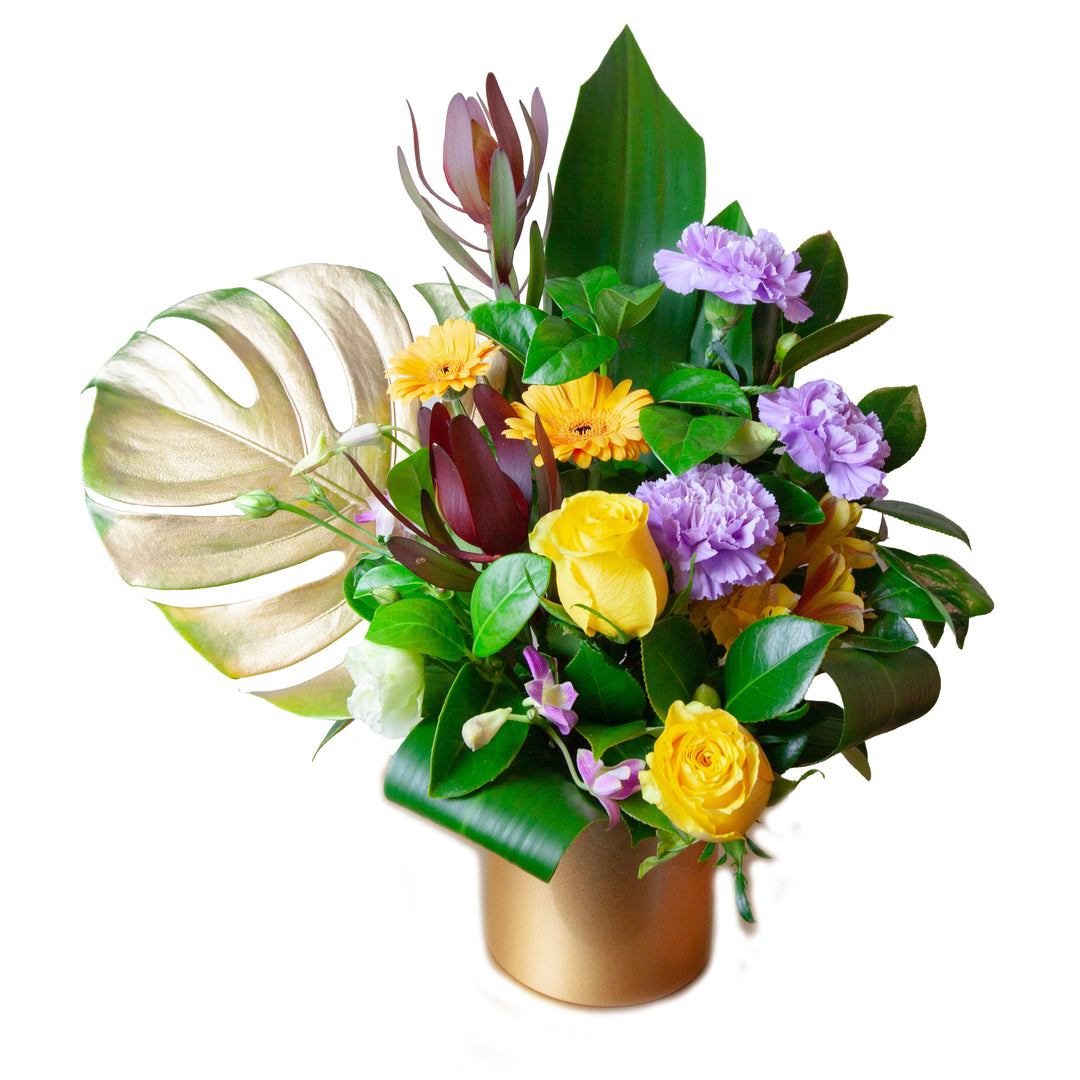 Sunlit Garden Arrangement featuring yellow roses, seasonal flowers, tropical foliage and botanical accents arranged in a modern gold vase.