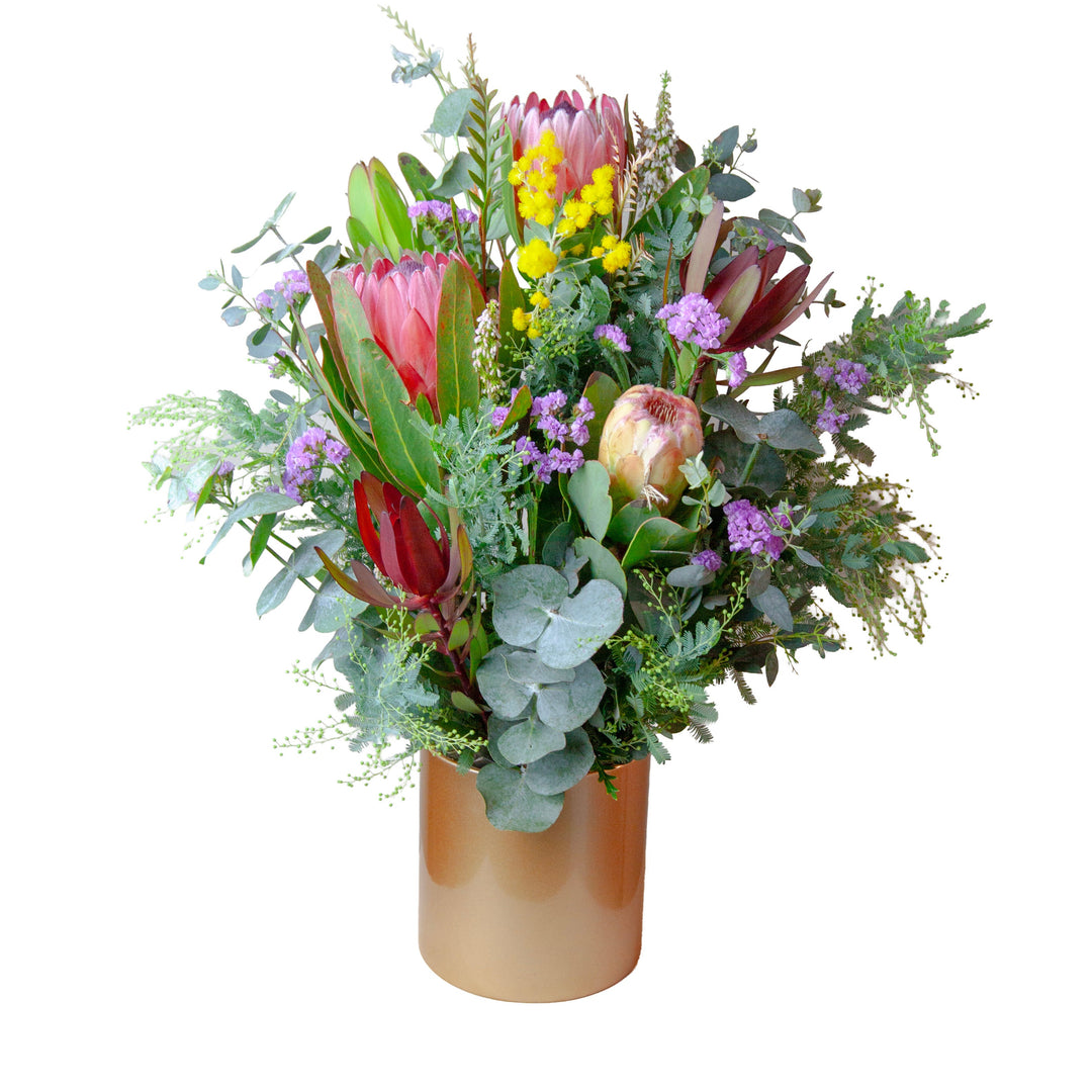 Golden Native Vase featuring pink proteas, Australian native flowers, seasonal wildflowers, eucalyptus and foliage arranged in a modern gold vase.