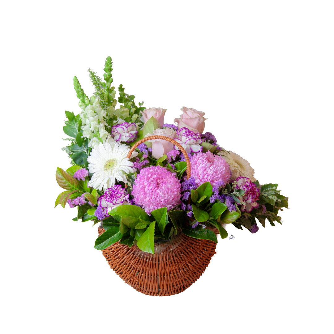 Sweet Lavender Basket in a woven basket featuring pink roses, lavender carnations, seasonal flowers and fresh garden-style foliage.