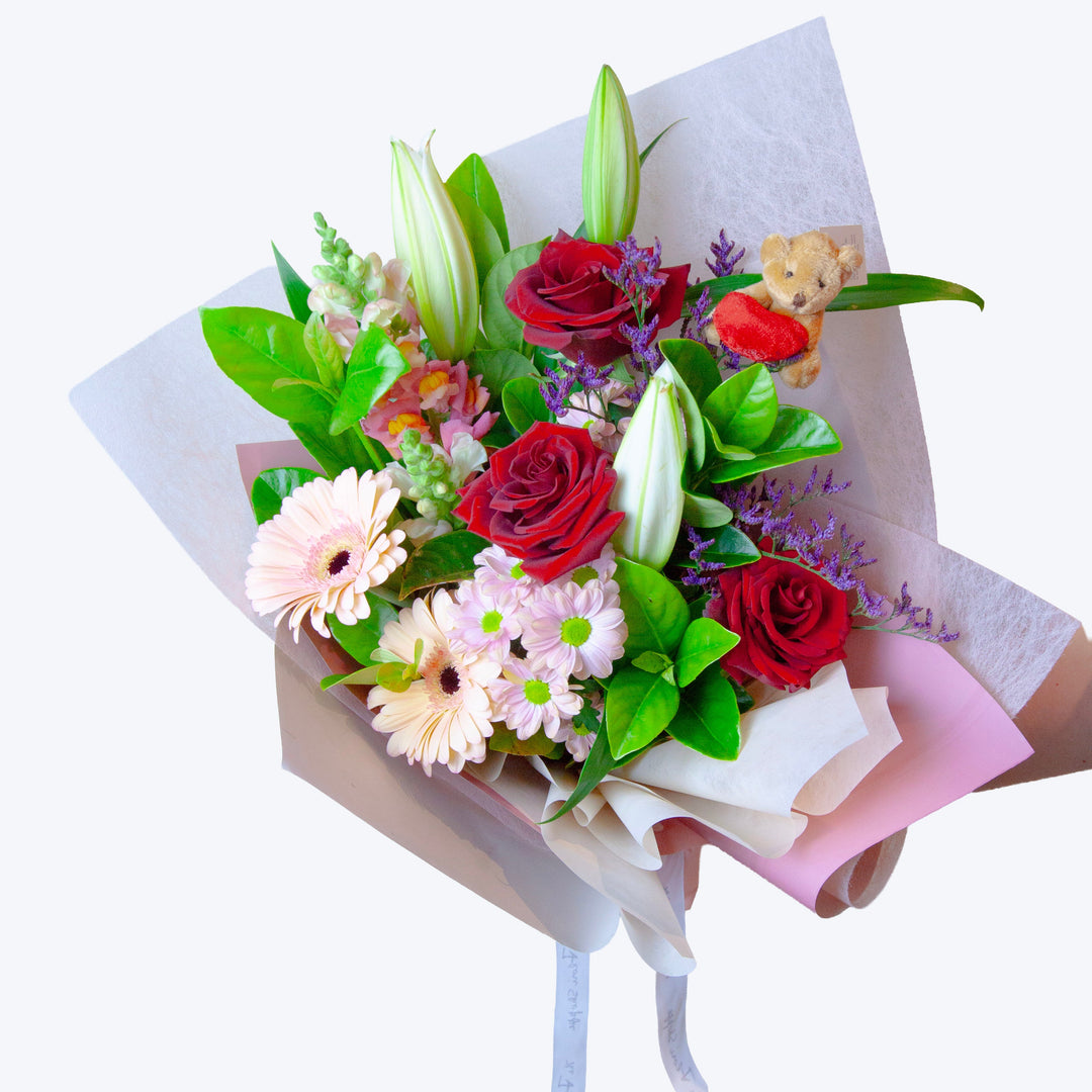 Love & Hugs bouquet featuring red roses, lilies, seasonal flowers and a teddy bear.