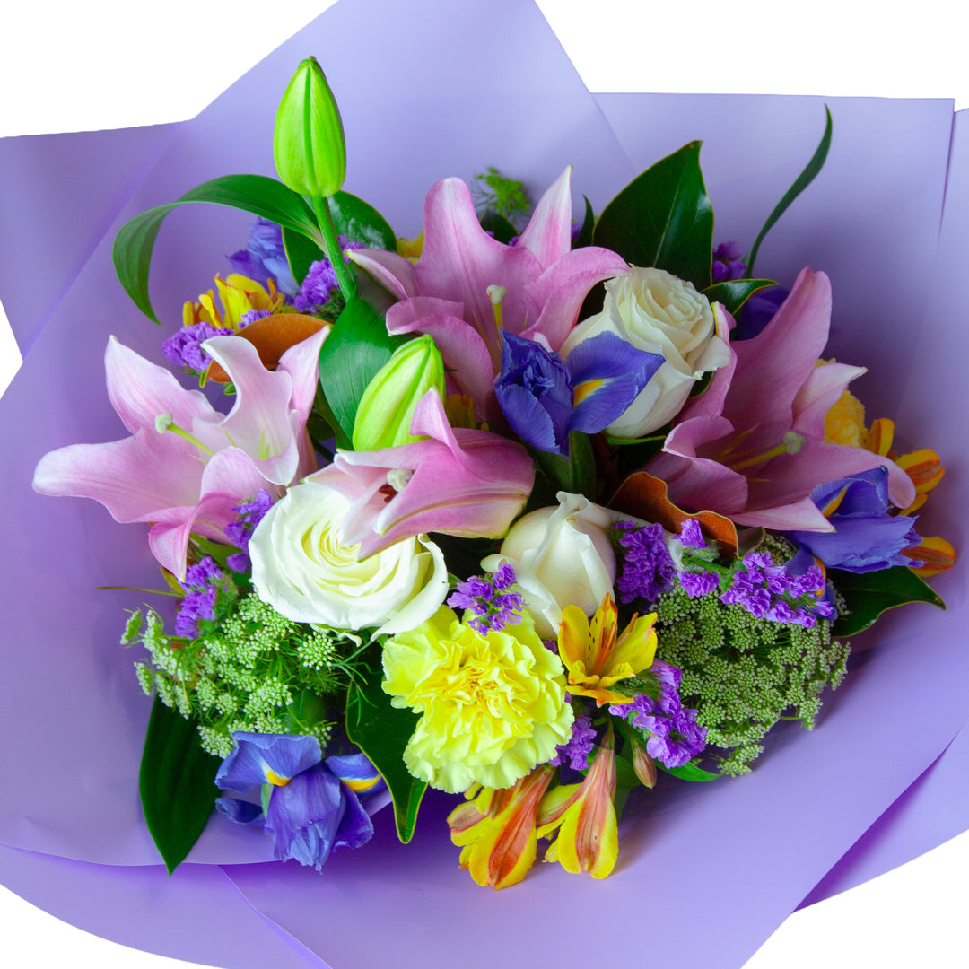 Pastel Harmony bouquet featuring pink lilies, white roses, blue irises and seasonal flowers, beautifully wrapped for gifting.