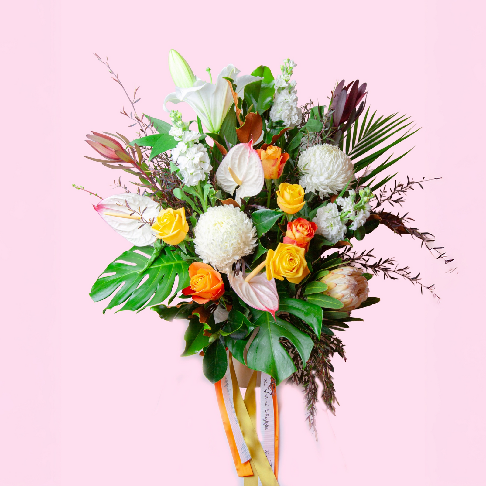 tropical flower arrangement with orange yellow roses white chrysanthemum monstera protea
