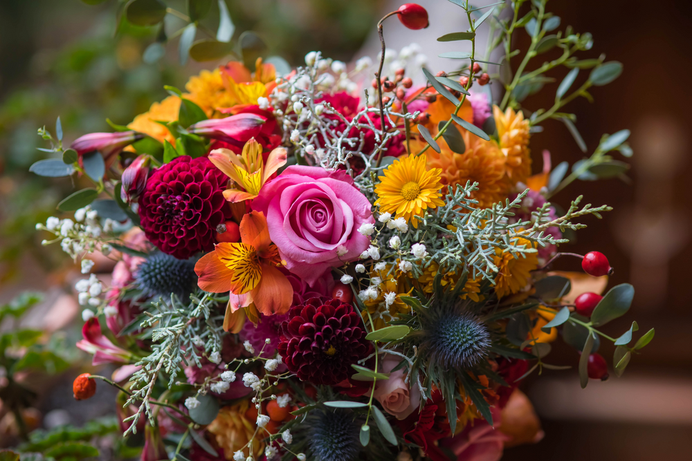 Colorful bouquet of flowers with pink roses, orange and yellow flowers, and greenery.
