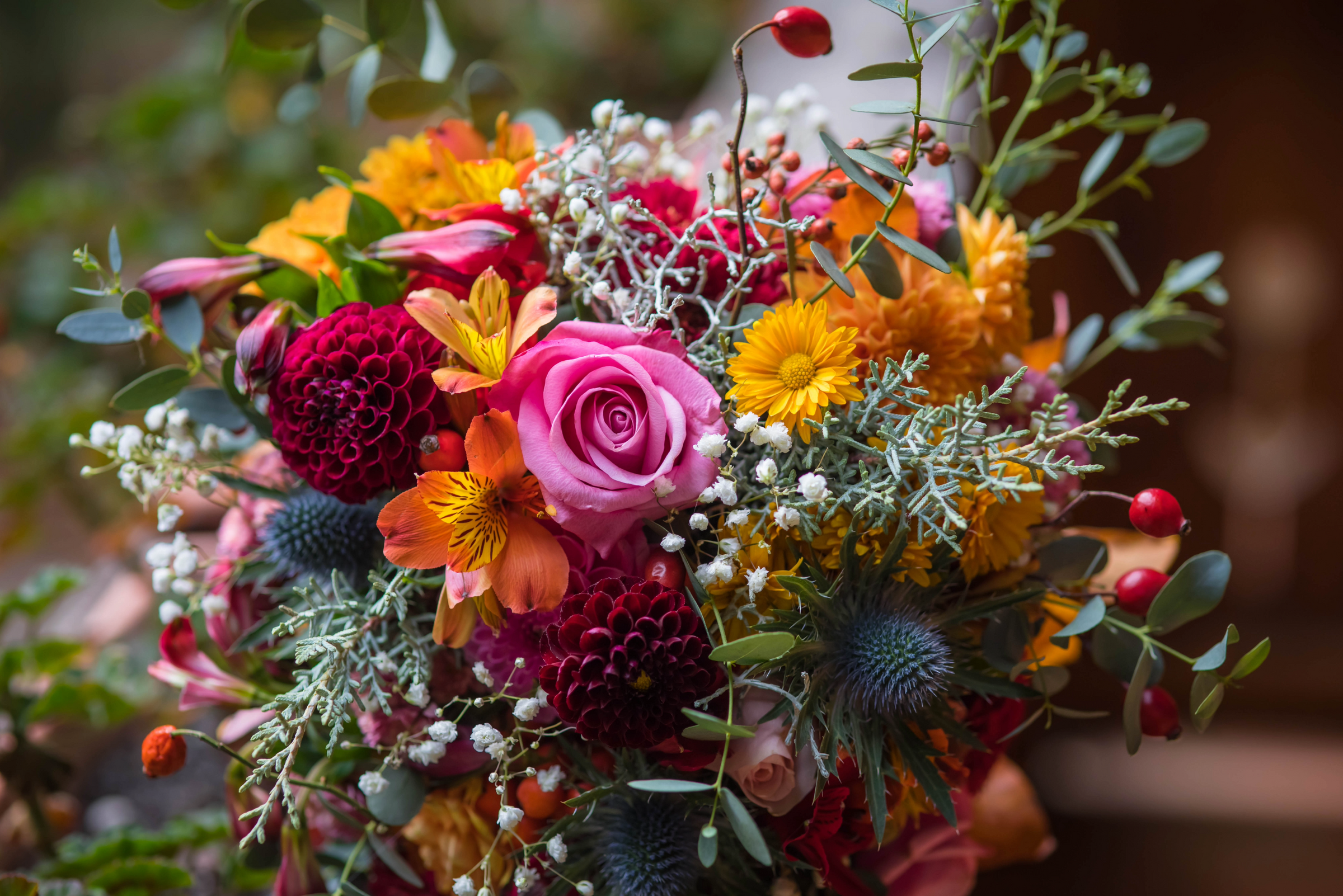 Colorful bouquet of flowers with pink roses, orange and yellow flowers, and greenery.