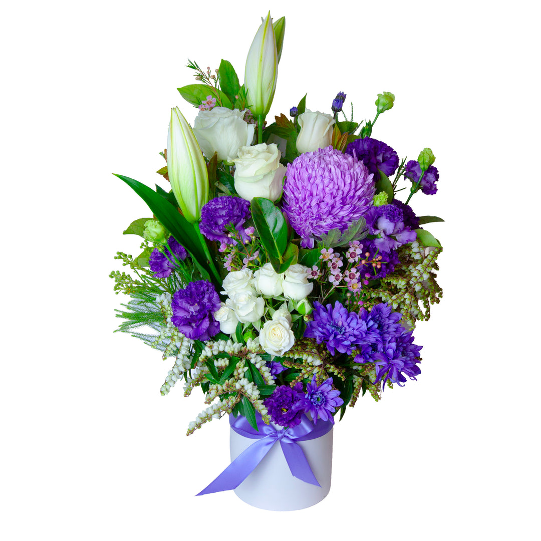 Lavender purple and white flower arrangement with white lilies, roses, disbud chrysanthemums in a white ceramic vase with purple ribbon