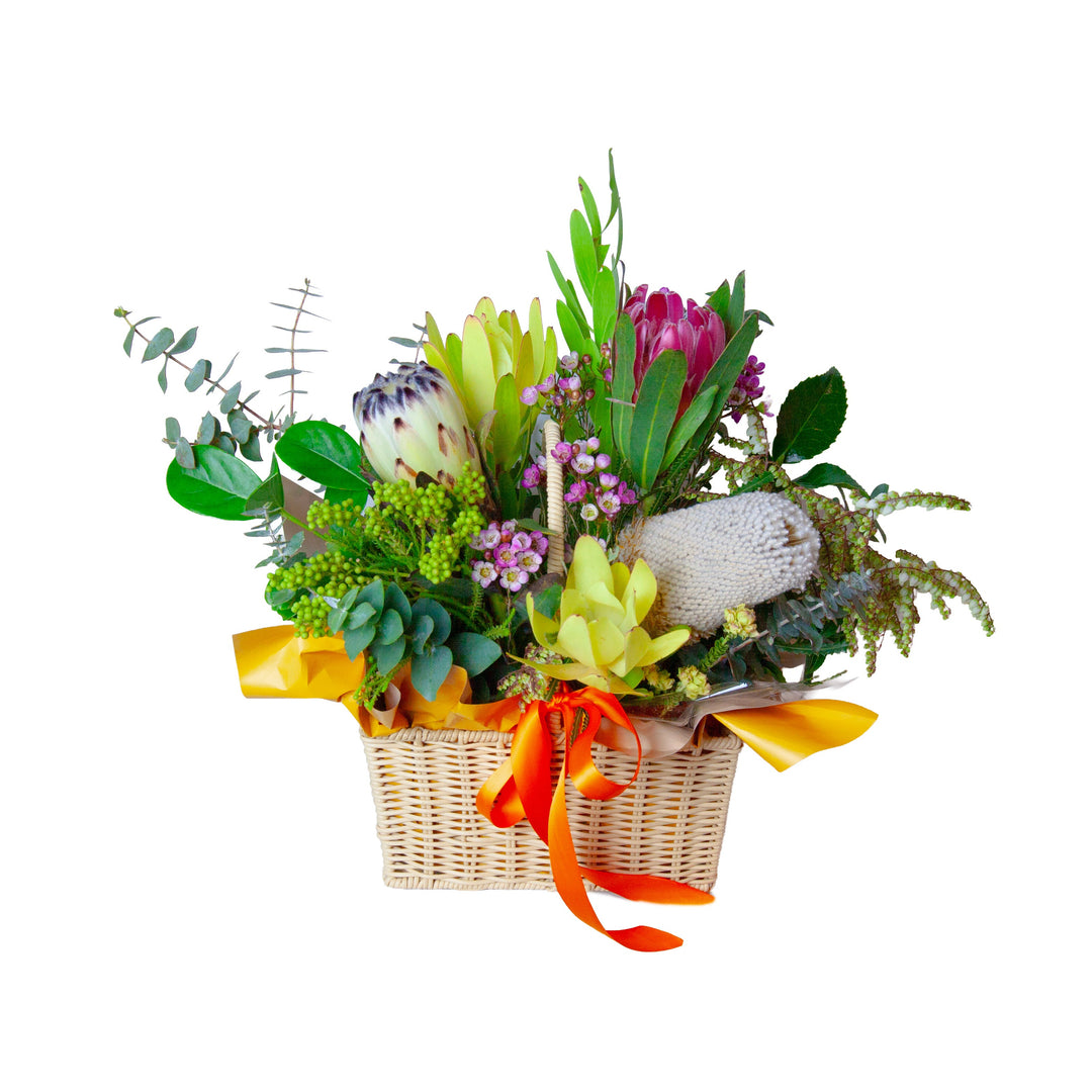 Native Charm Australian native flower basket featuring proteas, banksia, eucalyptus and vibrant yellow and pink blooms tied with an orange ribbon