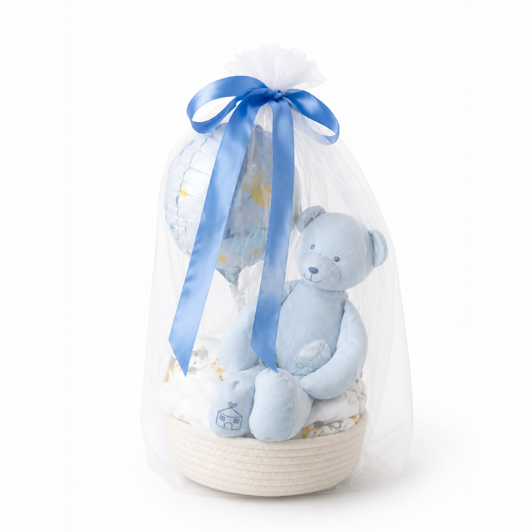 The Cheri Baby Boy Hamper by The Flori Shoppe, featuring a blue plush teddy bear, baby balloon, and essentials in a woven basket wrapped in tulle with a blue ribbon.